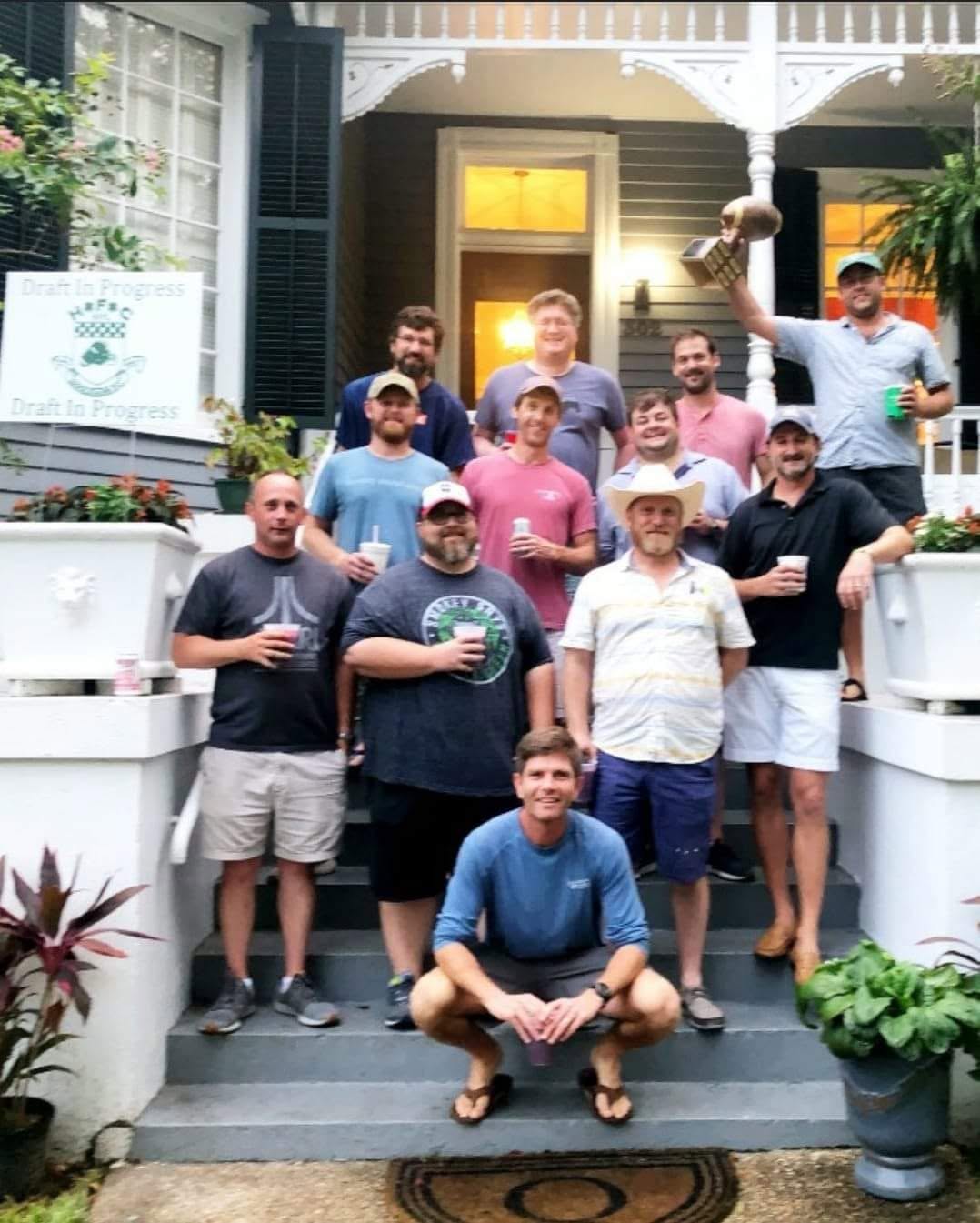 HFFL owners gathered on a porch while one owner raises the league trophy
